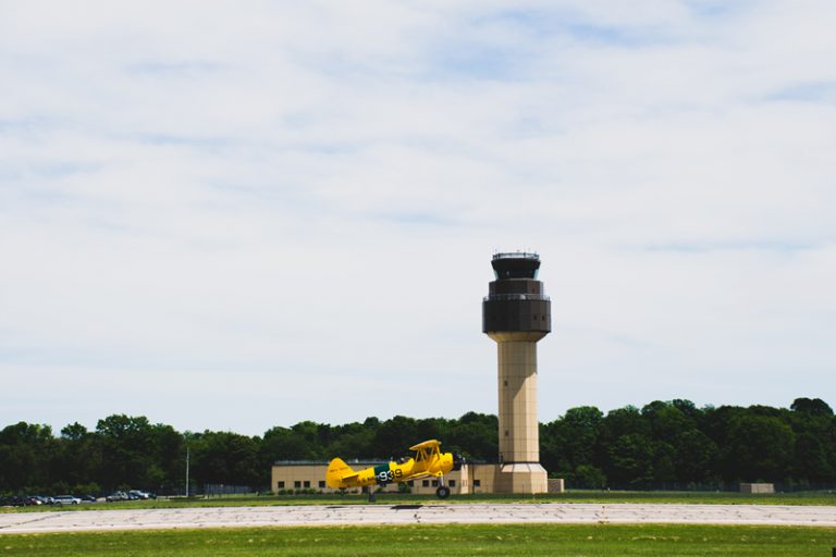 Side view of a small yellow plane in front of an Air Traffic Control Tower