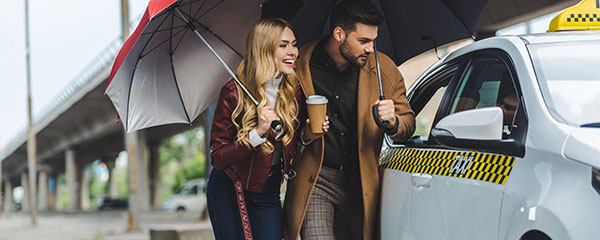 A couple laughing with umbrellas in their hands while trying to enter a taxi