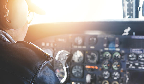 A photograph of a pilot inside their plane's cockpit with the sun shining in through the front window.